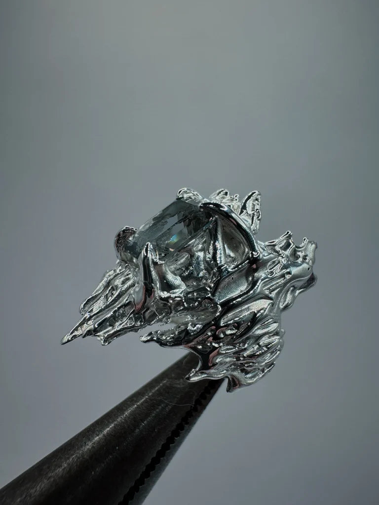 Gothic and organic style lost wax cast sterling silver ring with sharp edges. Four gothic style claws holding a grey lab grown nano crystal which was cast in place in the lost wax casting process. This is a view of the ring being held up with pliers.