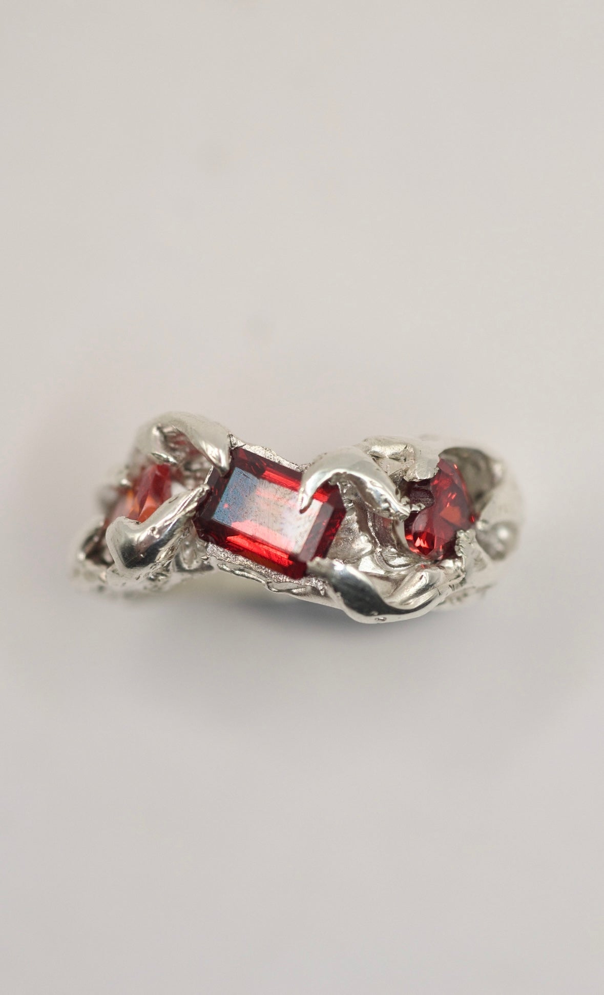 lost wax carved organic silver ring with textured claws holding three bright red ruby emerald cut gemstone created with the lost wax technique